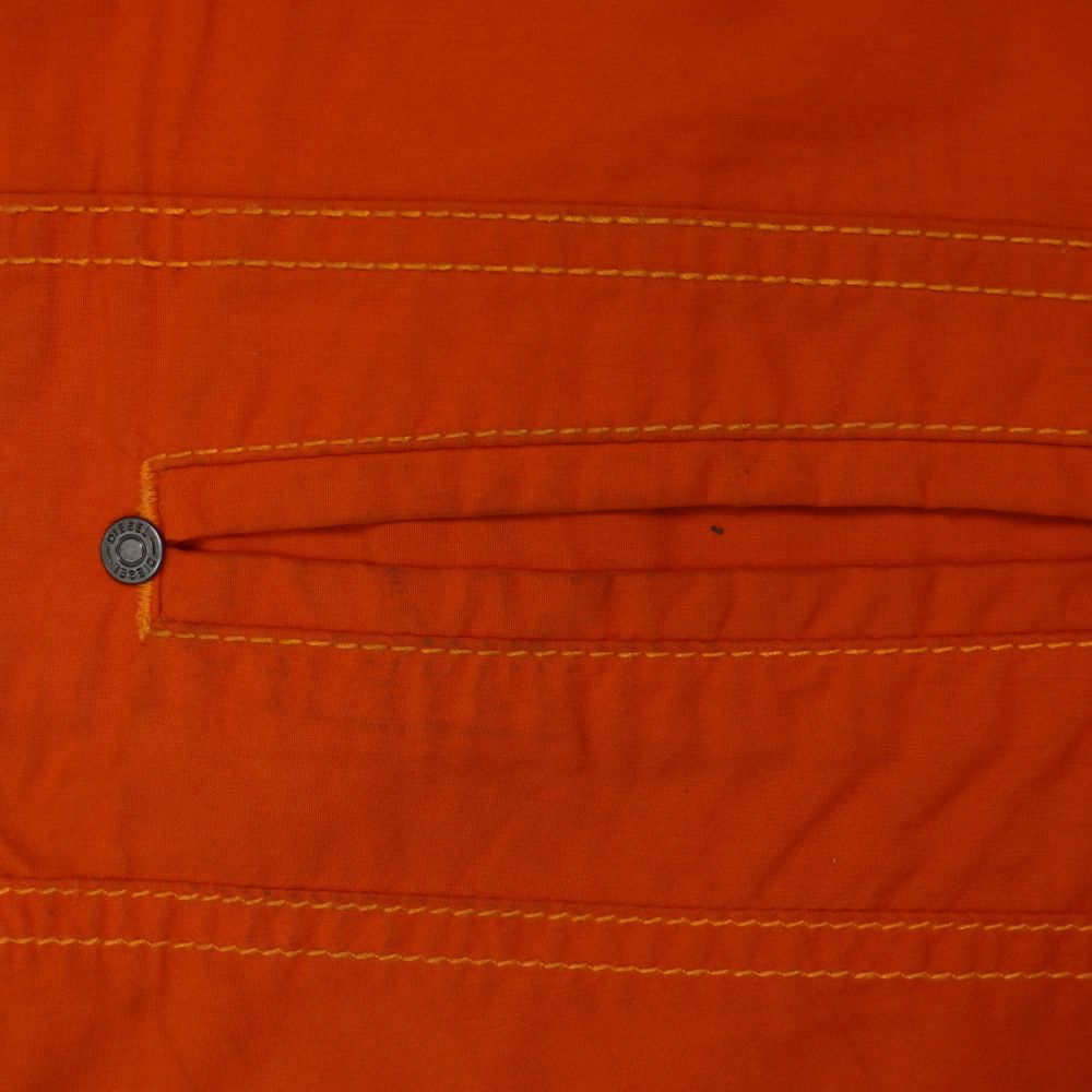 Foto macro di controllo qualità che mostra una piccolissima macchia scura puntiforme sul tessuto arancione dei pantaloni Diesel.