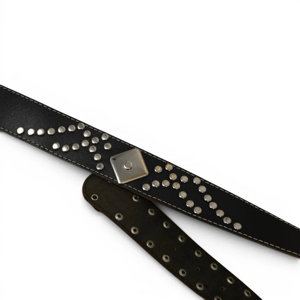 Particolare della cintura in pelle nera con decorazioni geometriche di borchie argentate a freccia e doppia fila di fori con occhielli metallici.