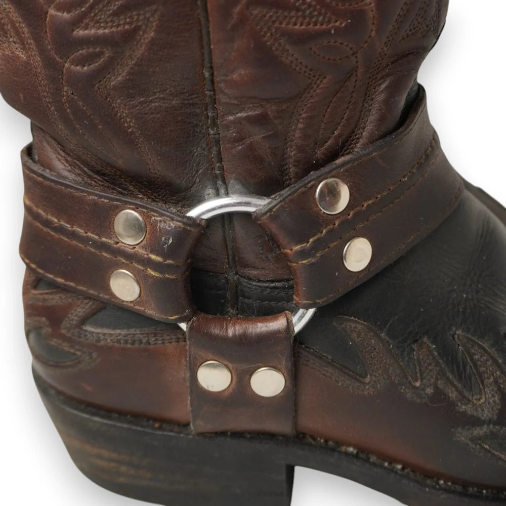 Primo piano ravvicinato dell'imbracatura laterale in pelle con anello e borchie metalliche sulla caviglia del biker boot.