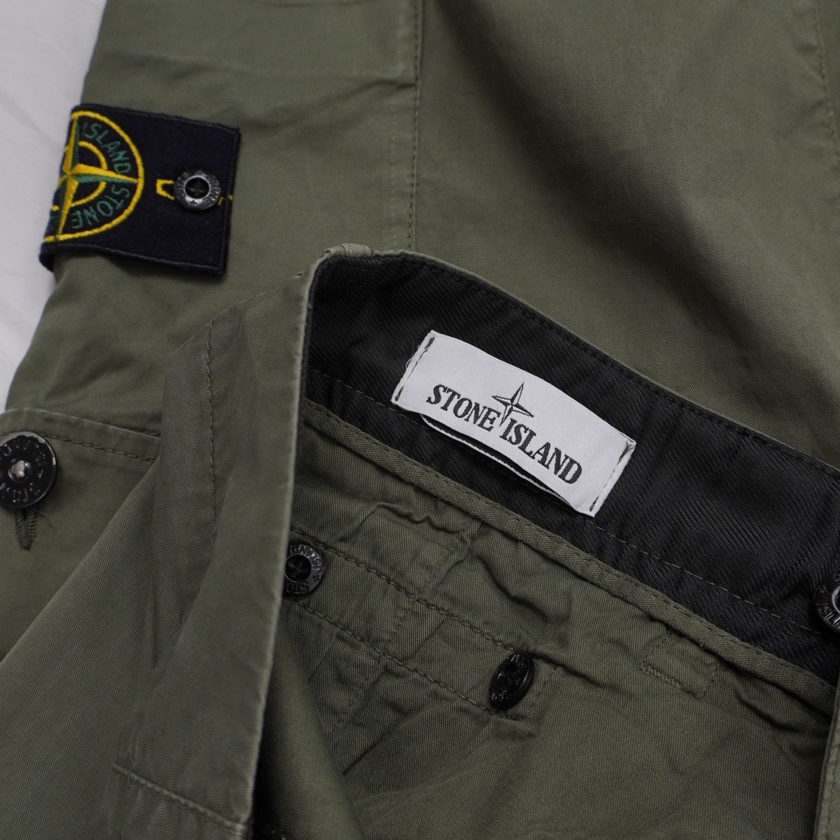 Inquadratura ravvicinata del badge rimovibile Stone Island applicato sulla tasca laterale e dell'etichetta interna del brand.