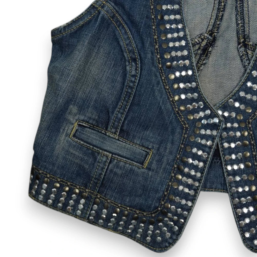 Primo piano delle borchie metalliche piatte argentate e degli strass sul profilo destro del gilet denim