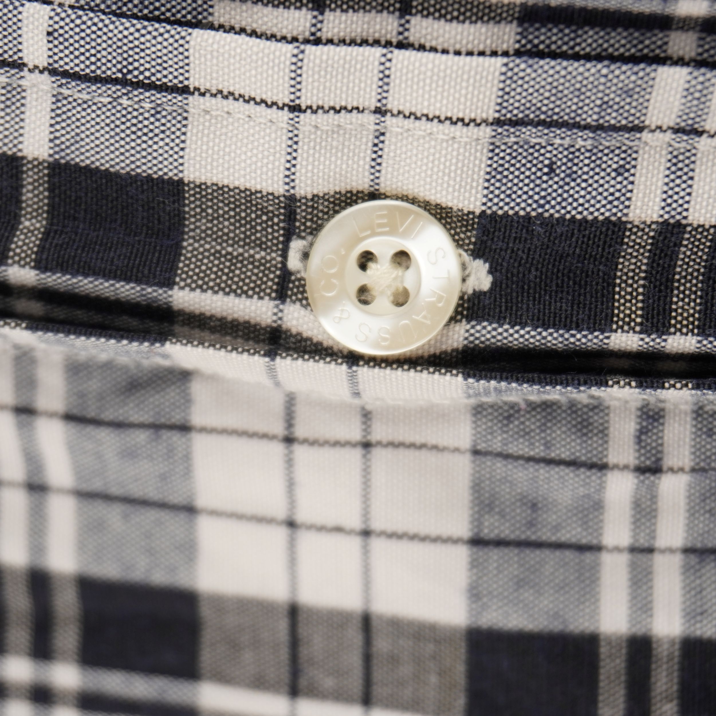 Dettaglio ravvicinato di un bottone bianco perlato cucito sulla patta frontale di una camicia vintage Levi's in cotone a scacchi.