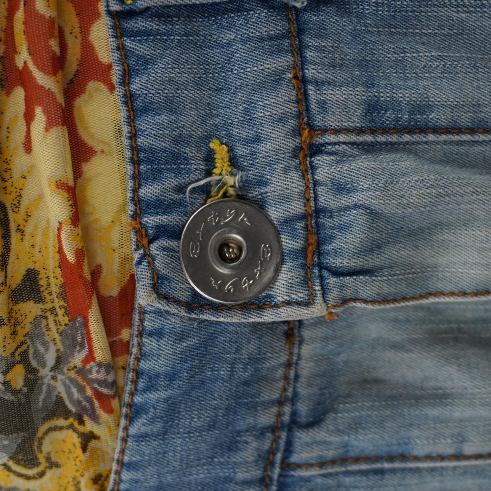 Macro del bottone metallico a chiodo argentato con incisione circolare in rilievo del logo Extyn Denim.