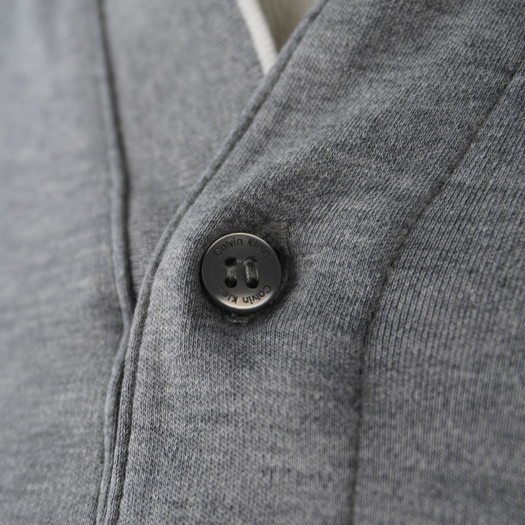 Close up del bottone originale nero con incisione laser del brand Calvin Klein e patta bianca a contrasto