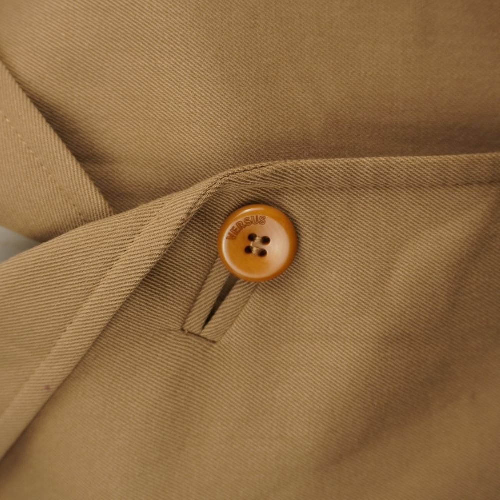 Dettaglio del bottone marrone con logo Versus inciso e trama diagonale del tessuto in misto lana.