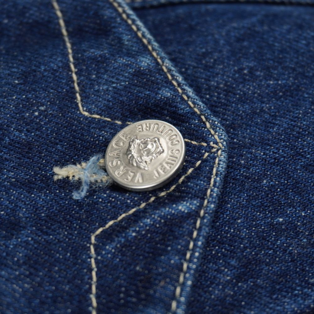 Macro del bottone metallico argentato con incisione della testa di Medusa sulla tasca della giacca denim vintage Versace.