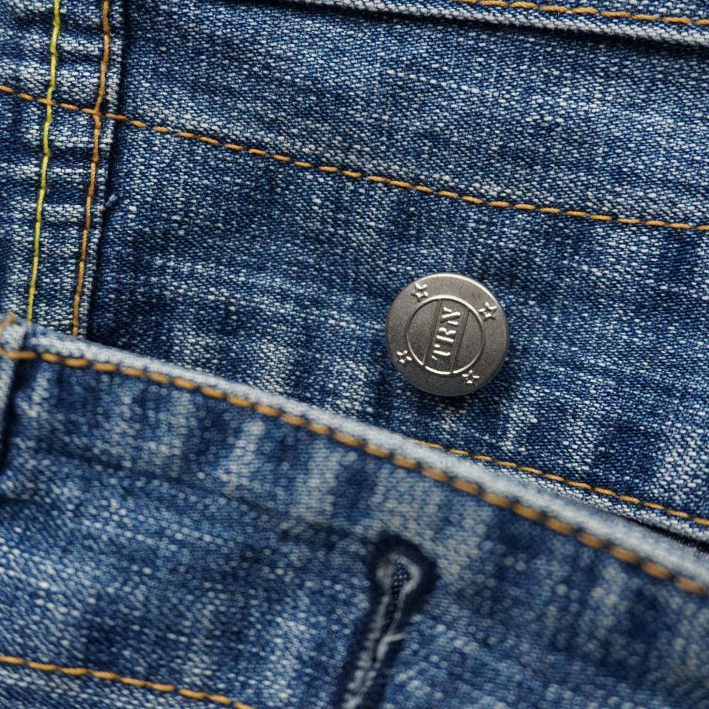 Primo piano del bottone a chiodo in metallo argentato satinato con monogramma TRN inciso su gilet denim vintage Terranova.