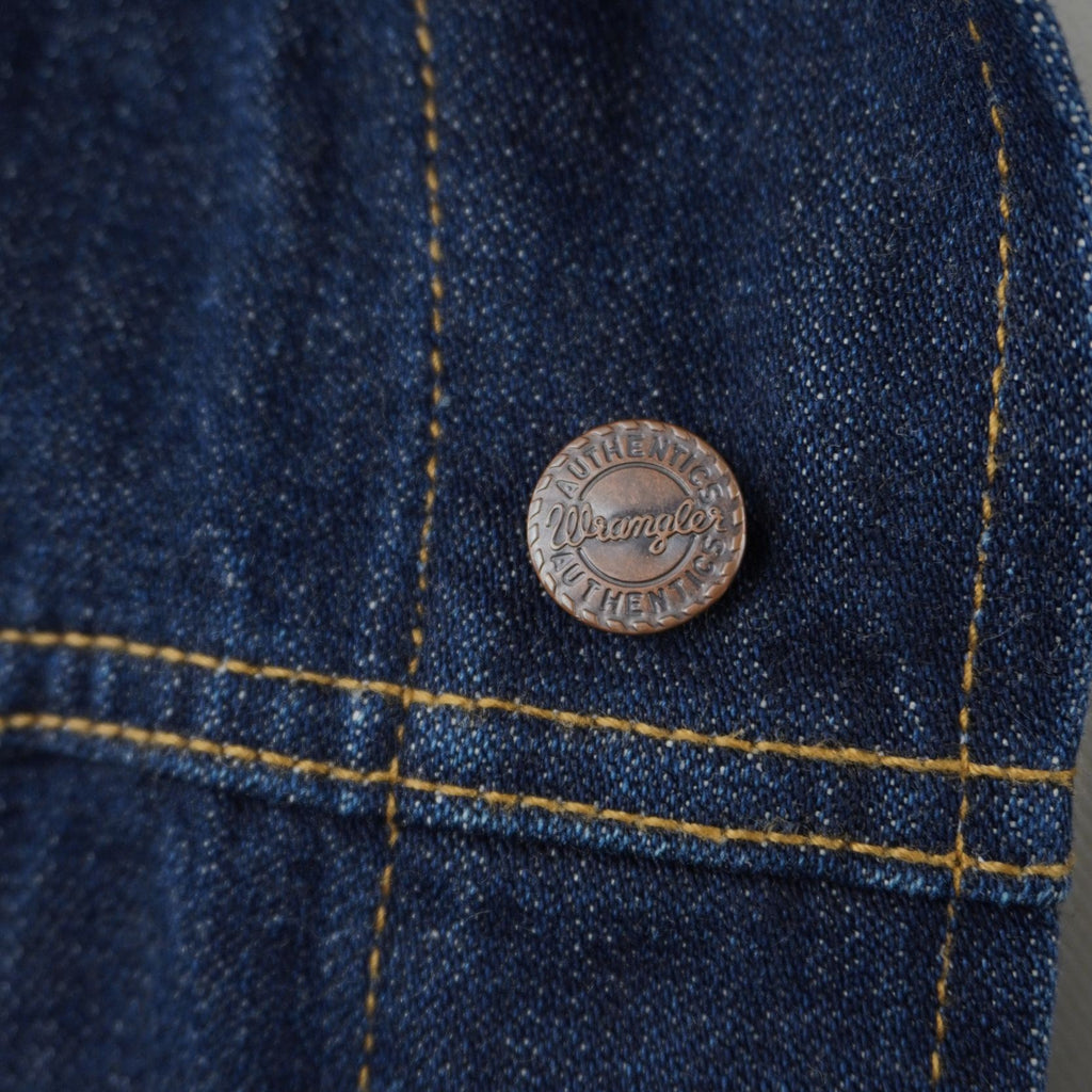 Macro di un bottone metallico originale Wrangler impresso a rilievo sul tessuto in denim rigido scuro.
