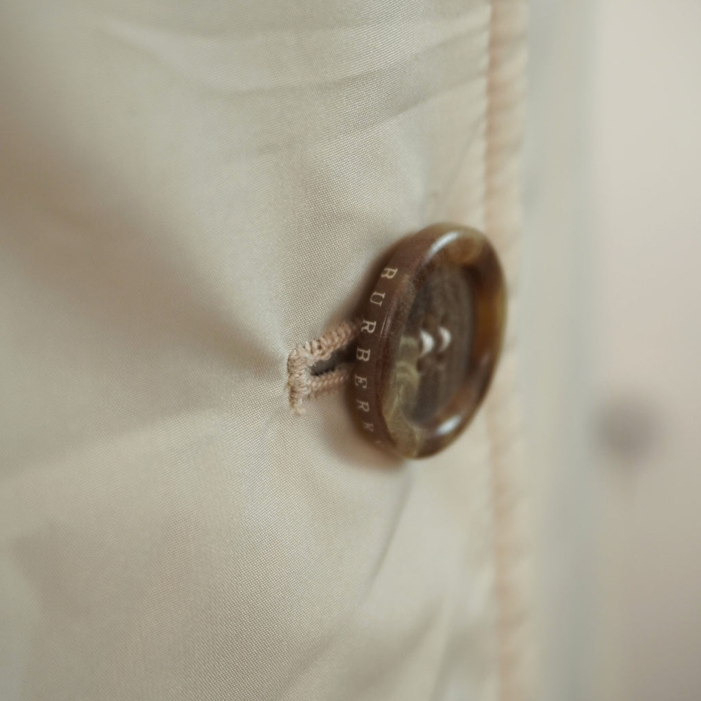 Particolare ravvicinato del bottone effetto tartarugato marrone con logo Burberry inciso e dettaglio della cucitura dell'asola.