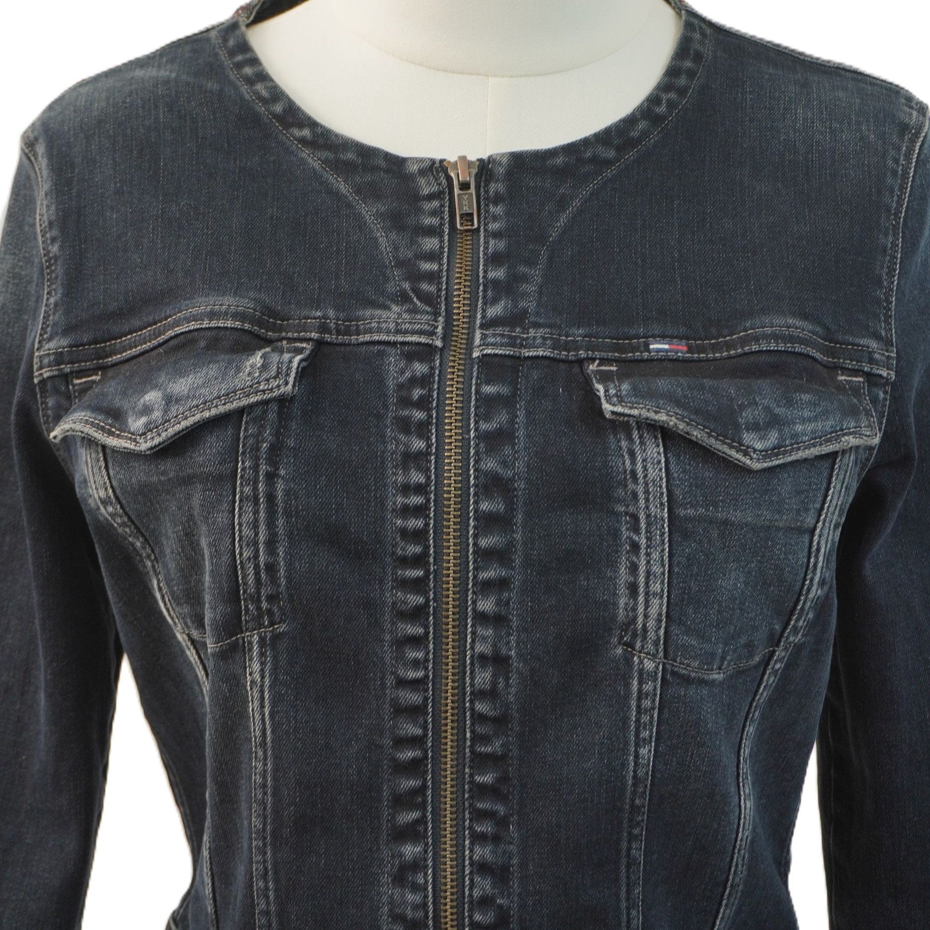 Primo piano del busto della giacca in denim scuro sul manichino, con focus sulle pattine delle tasche pettorali e sui dettagli delle cuciture verticali.
