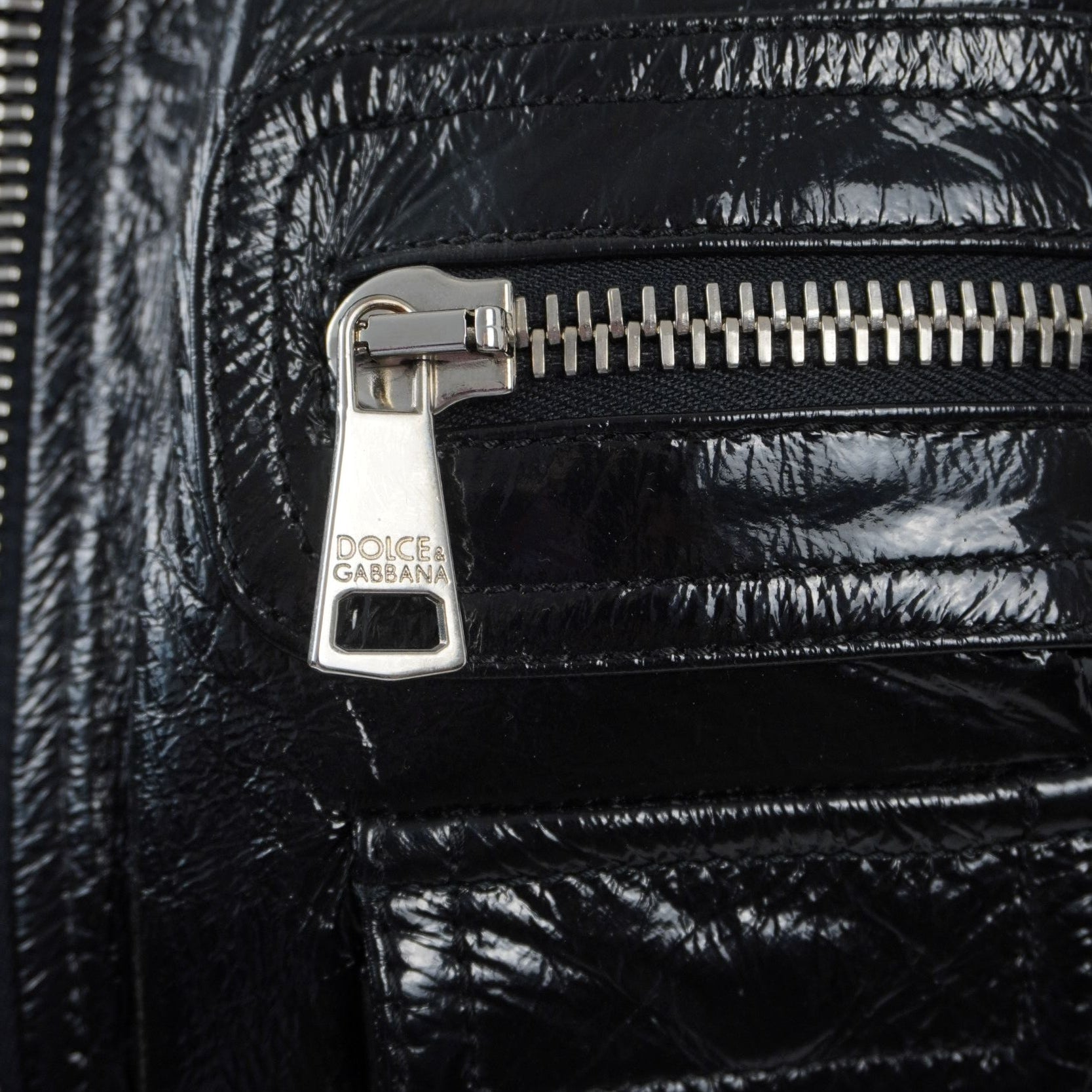 Inquadratura ravvicinata del cursore in metallo argentato lucido inciso con il logo ufficiale del brand Dolce & Gabbana.