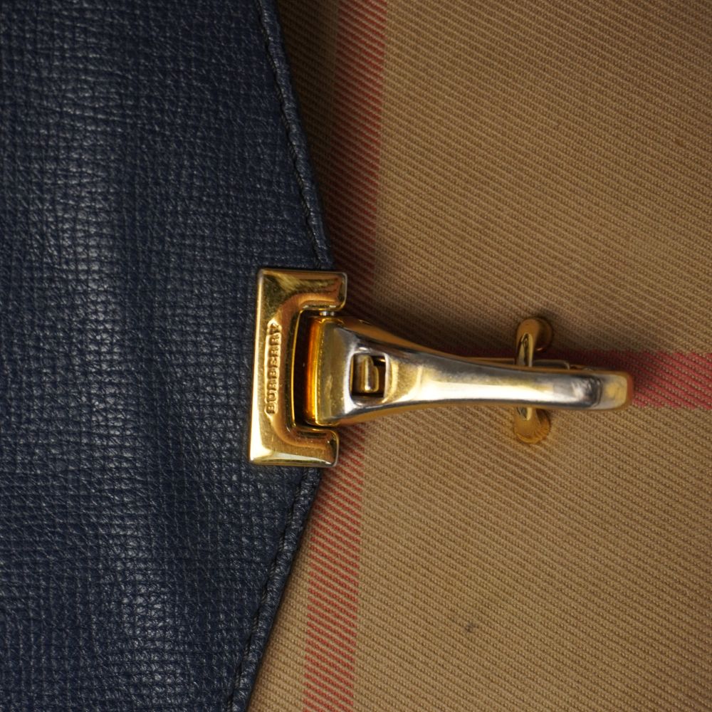 Primo piano della chiusura frontale a moschettone in metallo dorato con logo inciso su borsa Burberry Macken.