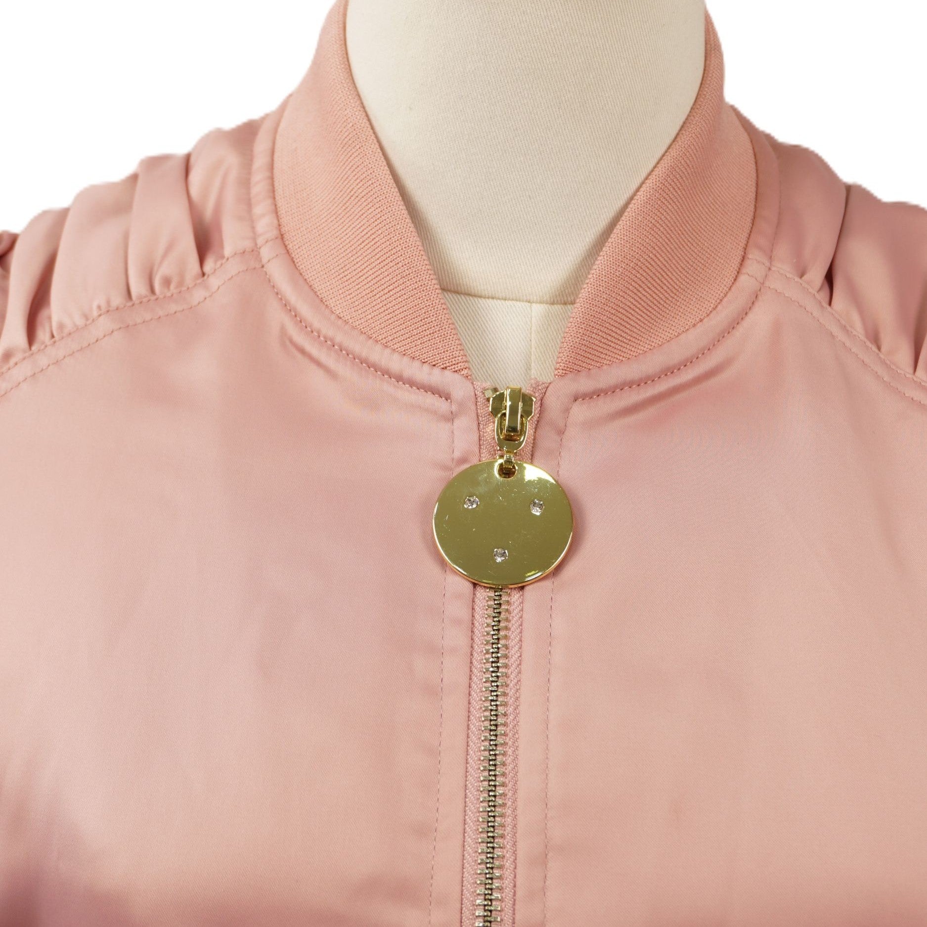 Primo piano del colletto elasticizzato a costine del bomber rosa, con focus sulla parte superiore della zip e sul medaglione dorato.
