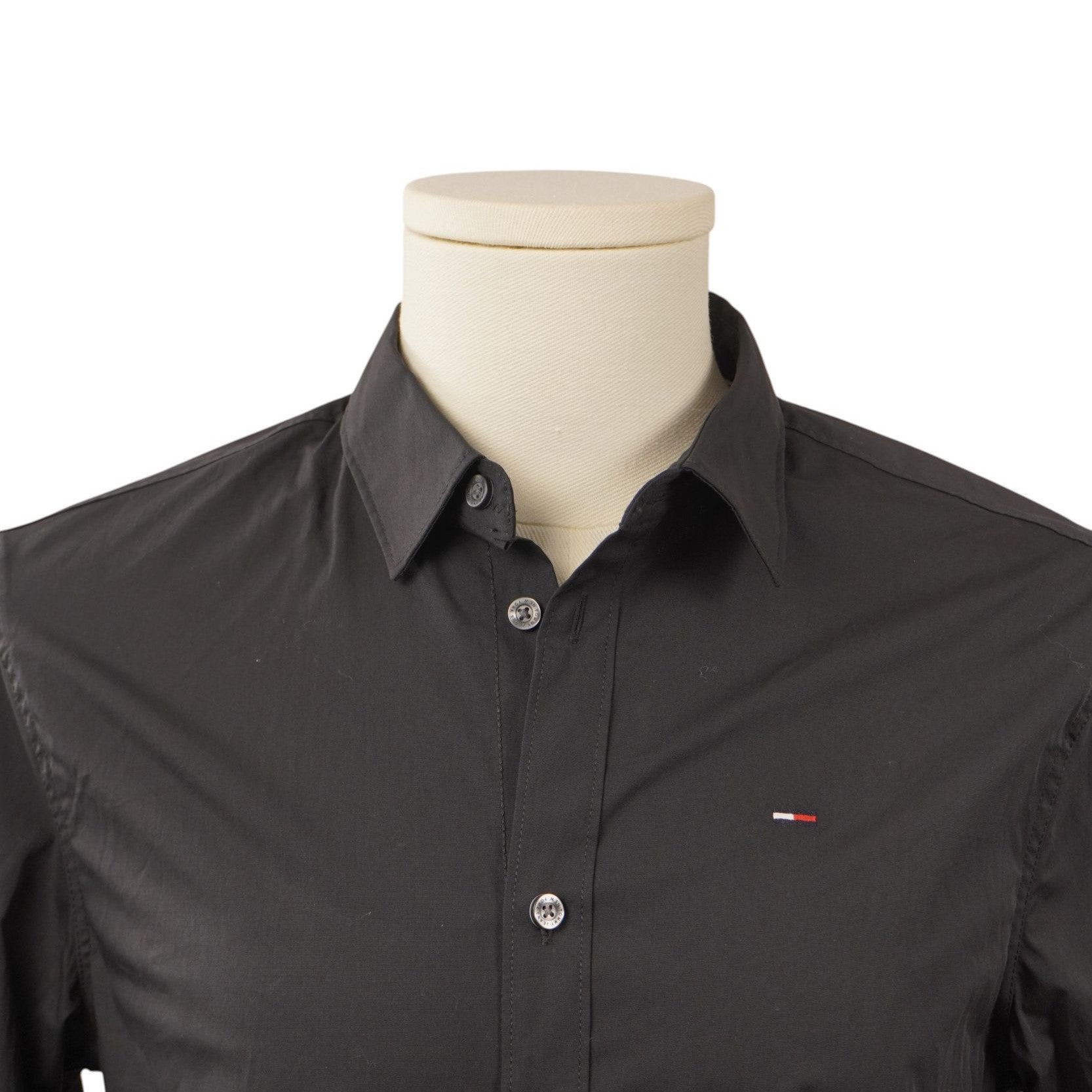 Primo piano frontale del colletto stile Kent e della parte superiore del busto della camicia abbottonata su manichino chiaro.