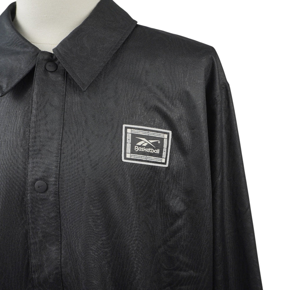 Primo piano frontale del colletto chiuso e della patch quadrata con logo Reebok Basketball sul lato sinistro della giacca.