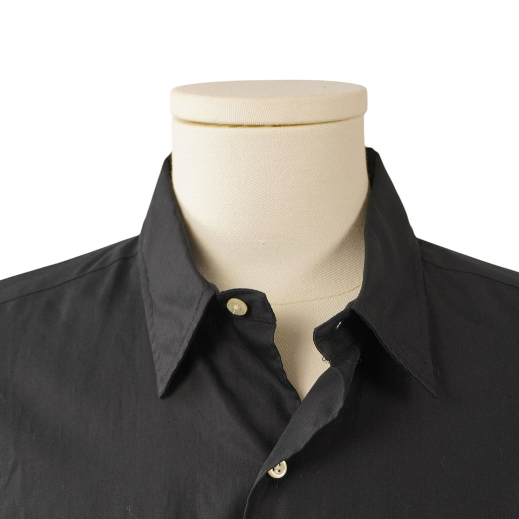 Primo piano frontale del colletto classico a punta e dello scollo di una camicia nera abbottonata su manichino.
