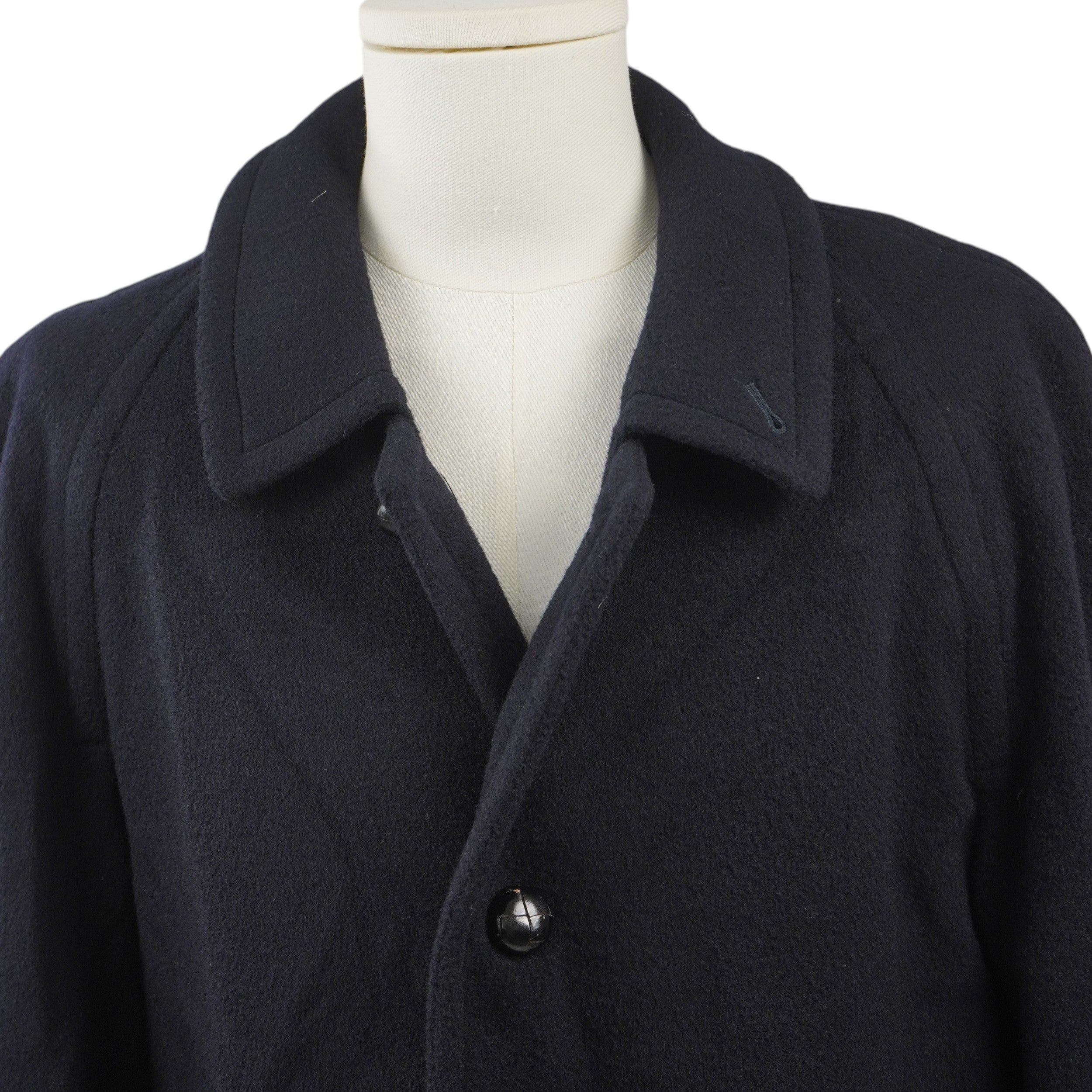 Primo piano frontale del colletto a camicia e dei primi bottoni scuri di chiusura del cappotto vintage blu navy.