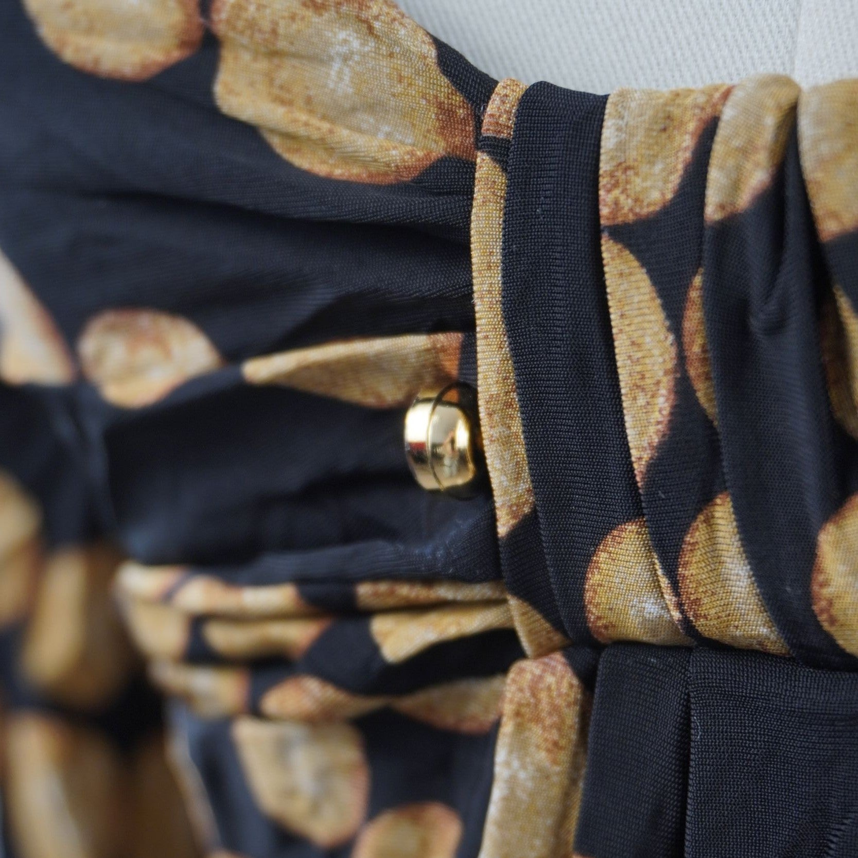 Close-up delle pieghe centrali sul décolleté impreziosite da un piccolo dettaglio metallico dorato firmato Roberto Cavalli.