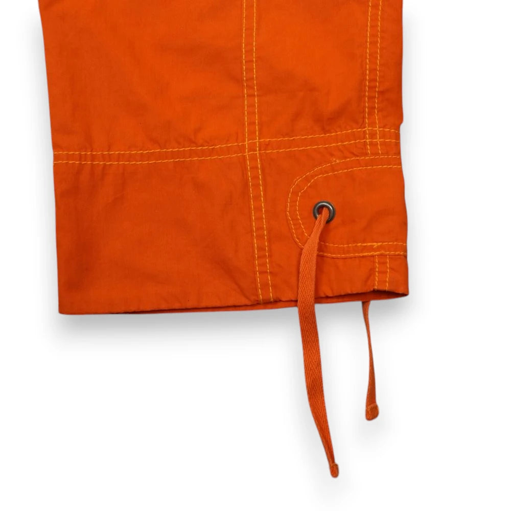 Dettaglio dell'orlo inferiore dei pantaloni capri Diesel arancioni con occhiello metallico e lacci piatti della coulisse.