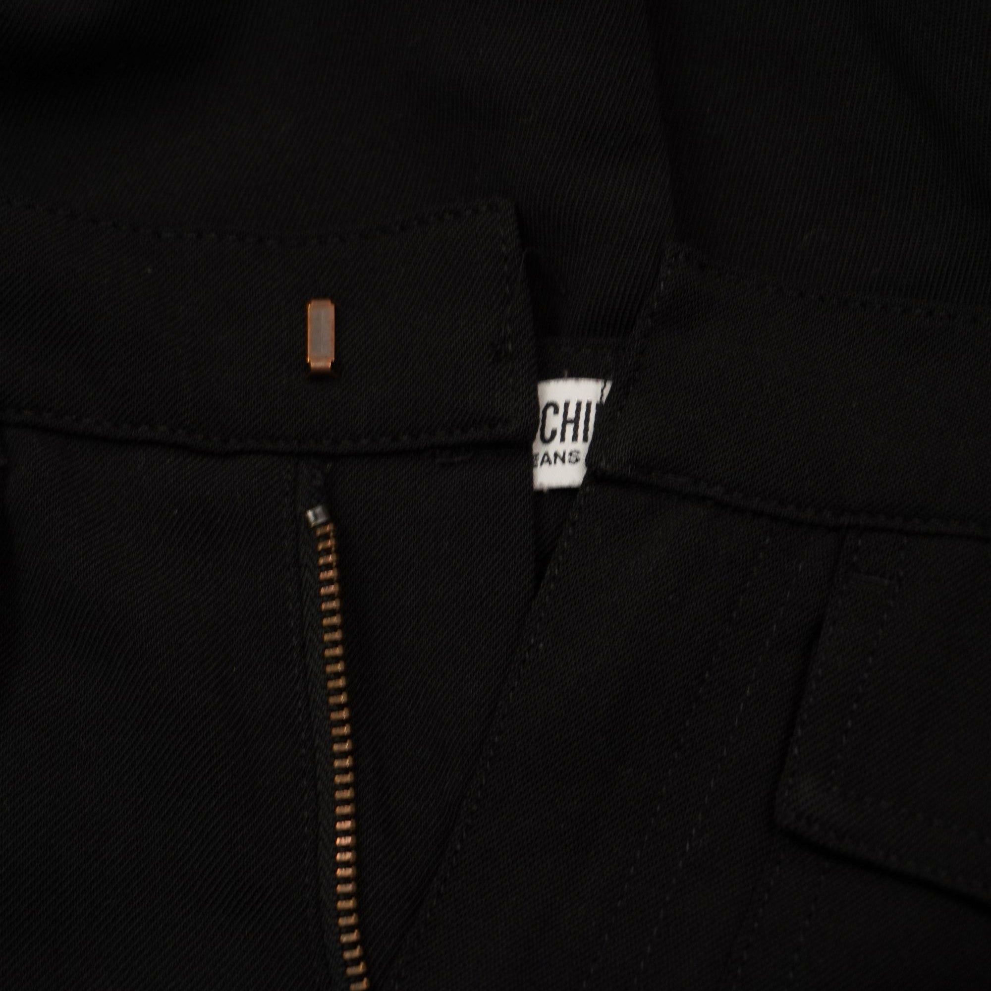 Vista ravvicinata delle finiture sartoriali e della fettuccia interna della cerniera lampo dei pantaloni neri.
