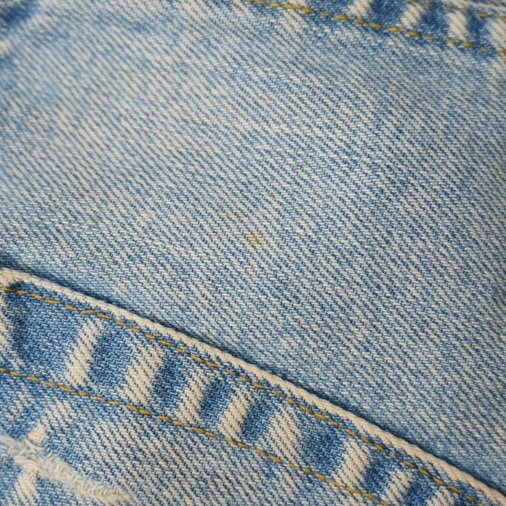 Foto macro di dettaglio che mostra una piccola e lieve macchia superficiale sul tessuto denim chiaro della gonna.