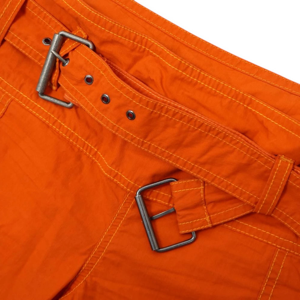 Dettaglio del fascione in vita dei pantaloni Diesel con doppia fibbia quadrata in metallo e occhielli sulla cintura arancione.