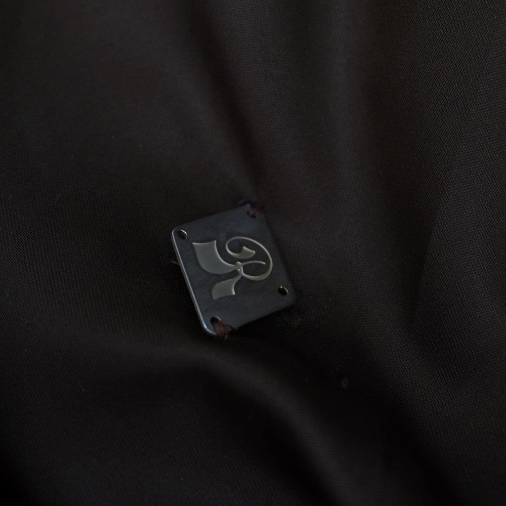 Primo piano della fodera interna scura del cappotto che mostra un dettaglio ricamato o un piccolo logo geometrico.