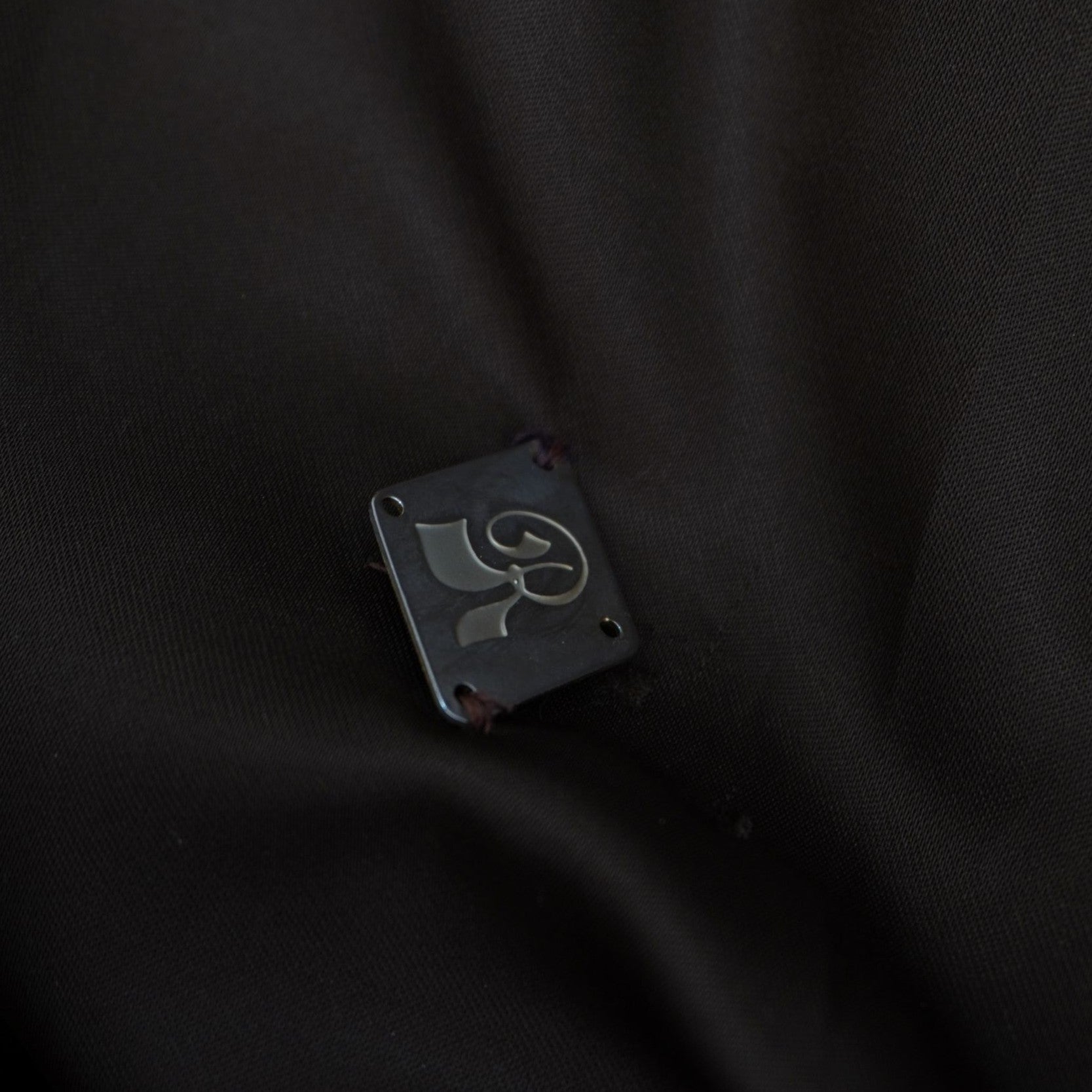 Primo piano della fodera interna scura del cappotto che mostra un dettaglio ricamato o un piccolo logo geometrico.