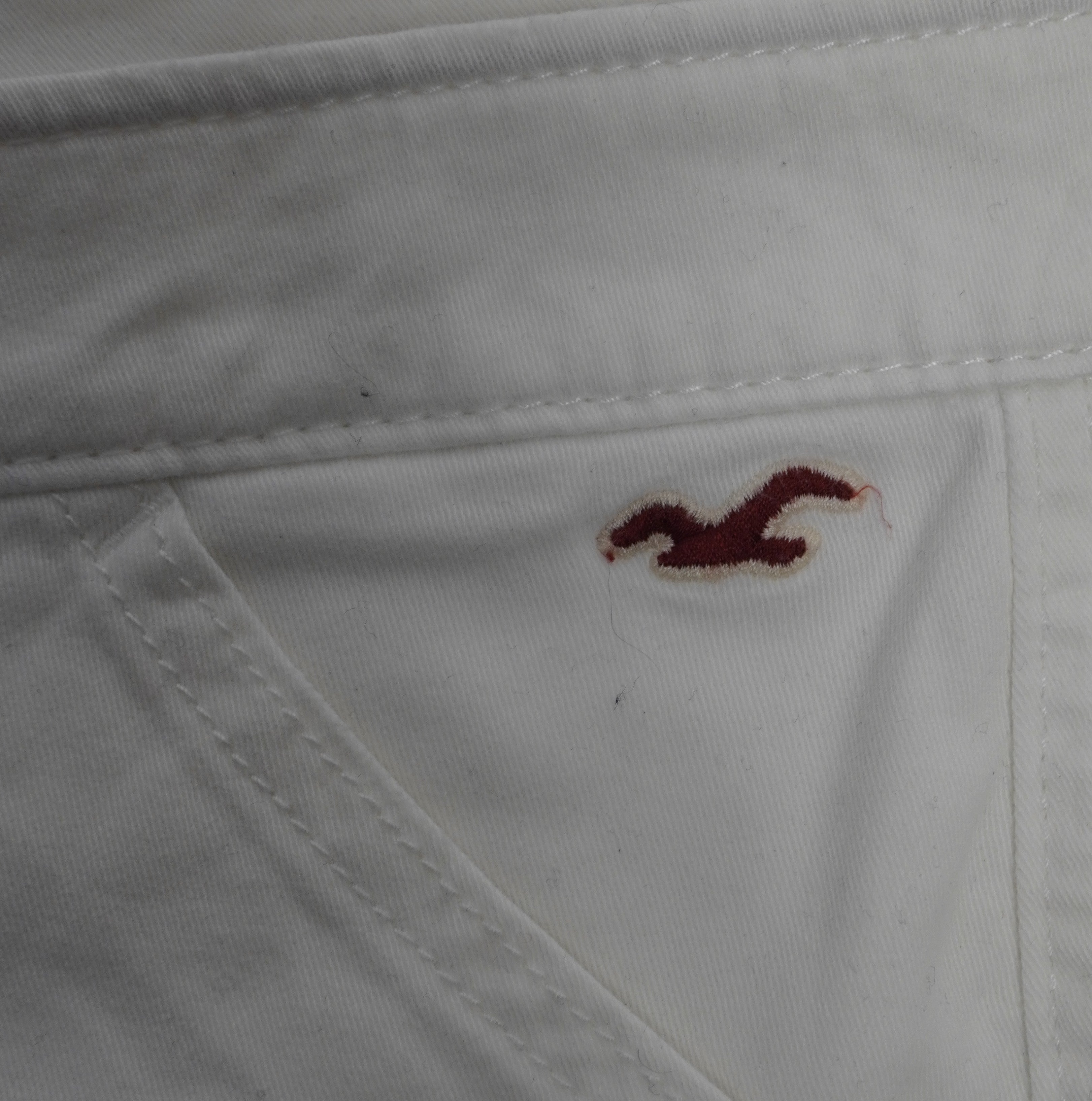  Inquadratura ravvicinata del logo con il gabbiano Hollister ricamato in filo bordeaux sulla tasca anteriore sinistra.