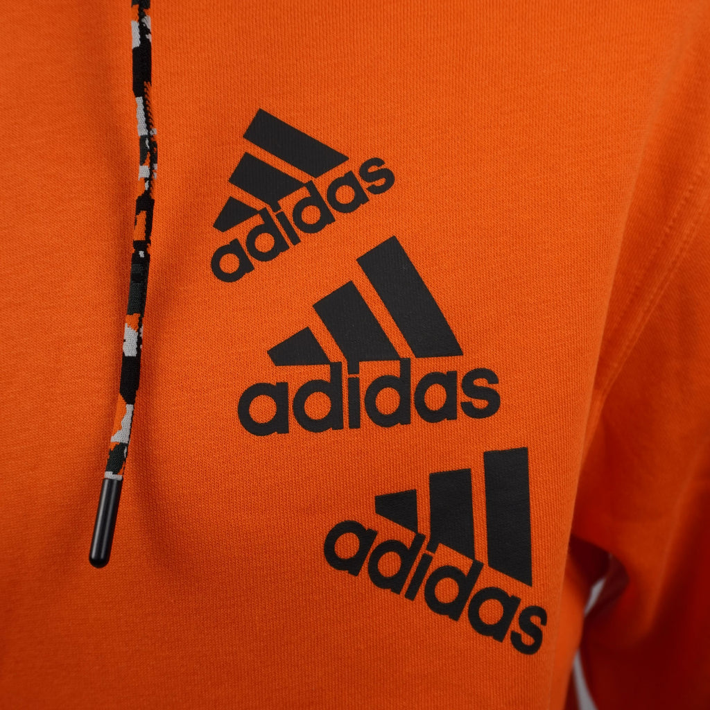 Primo piano del triplo logo adidas Badge of Sport impilato sul petto della felpa arancione.
