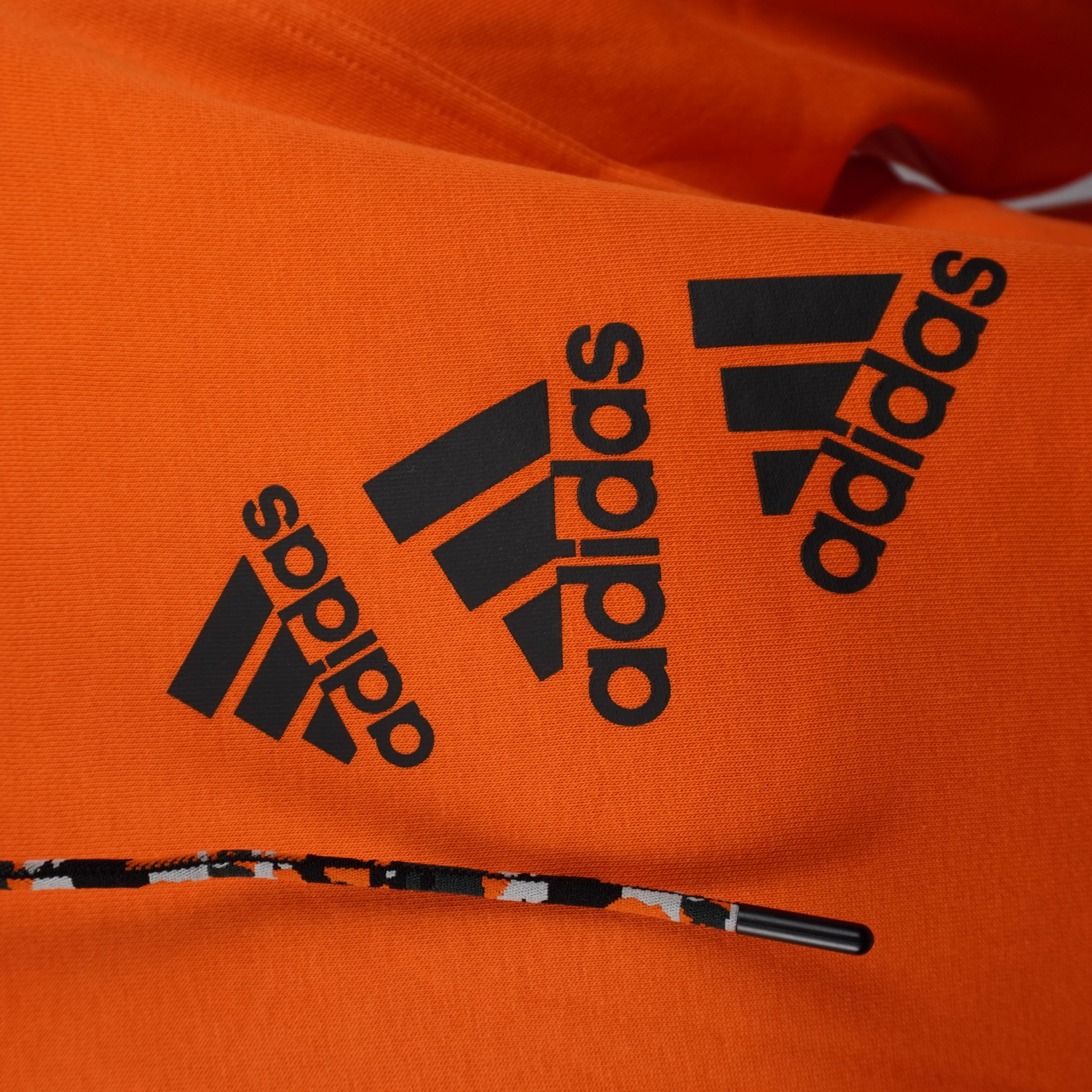 Primo piano del triplo logo adidas Badge of Sport impilato sul petto della felpa arancione.