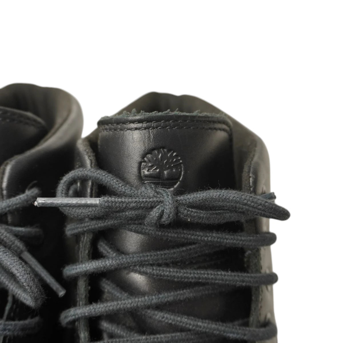 Zoom ravvicinato sulla linguetta anteriore con il logo dell'albero Timberland impresso a caldo e stringhe intrecciate nere.