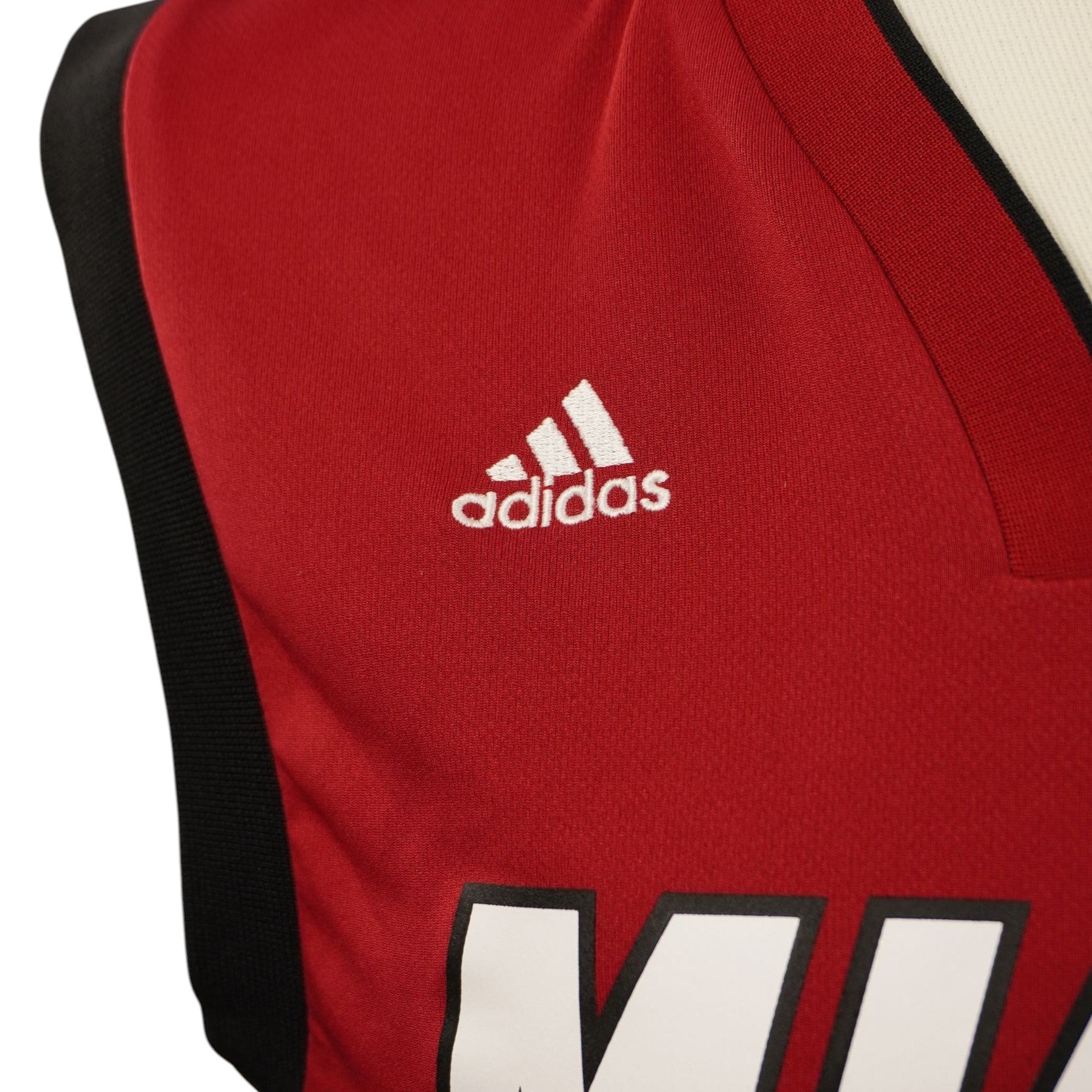 Inquadratura ravvicinata della spalla destra della maglia con il logo Adidas ricamato in filo bianco su tessuto tecnico rosso.
