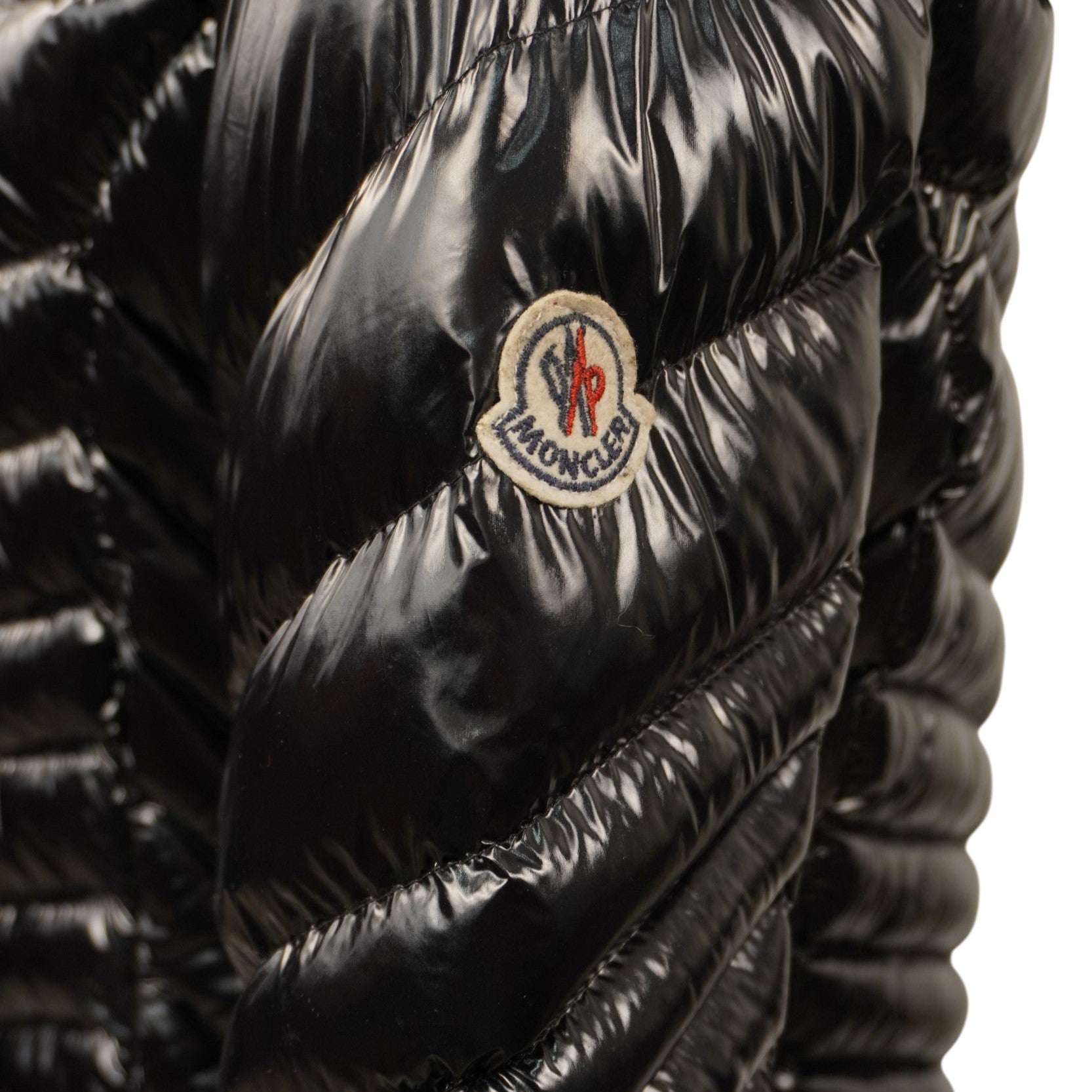 Dettaglio ravvicinato dell'iconico logo Moncler in feltro bianco, rosso e blu cucito sulla manica sinistra in nylon laccato nero.