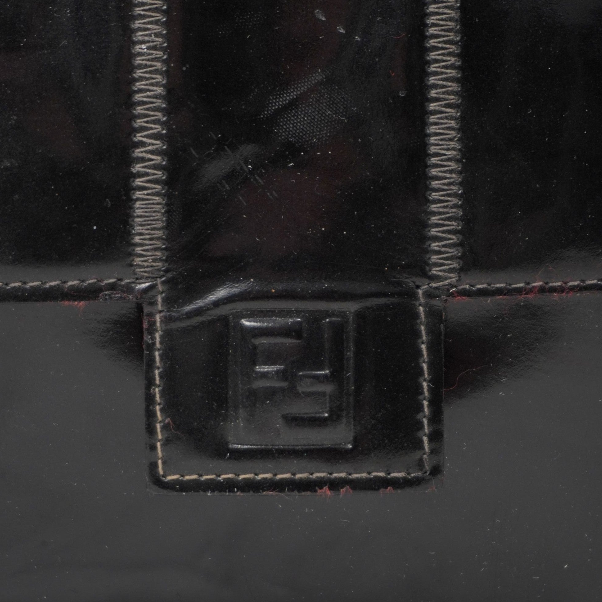 Primo piano del logo iconico FF di Fendi impresso a rilievo sulla patta frontale della borsa in pelle lucida.