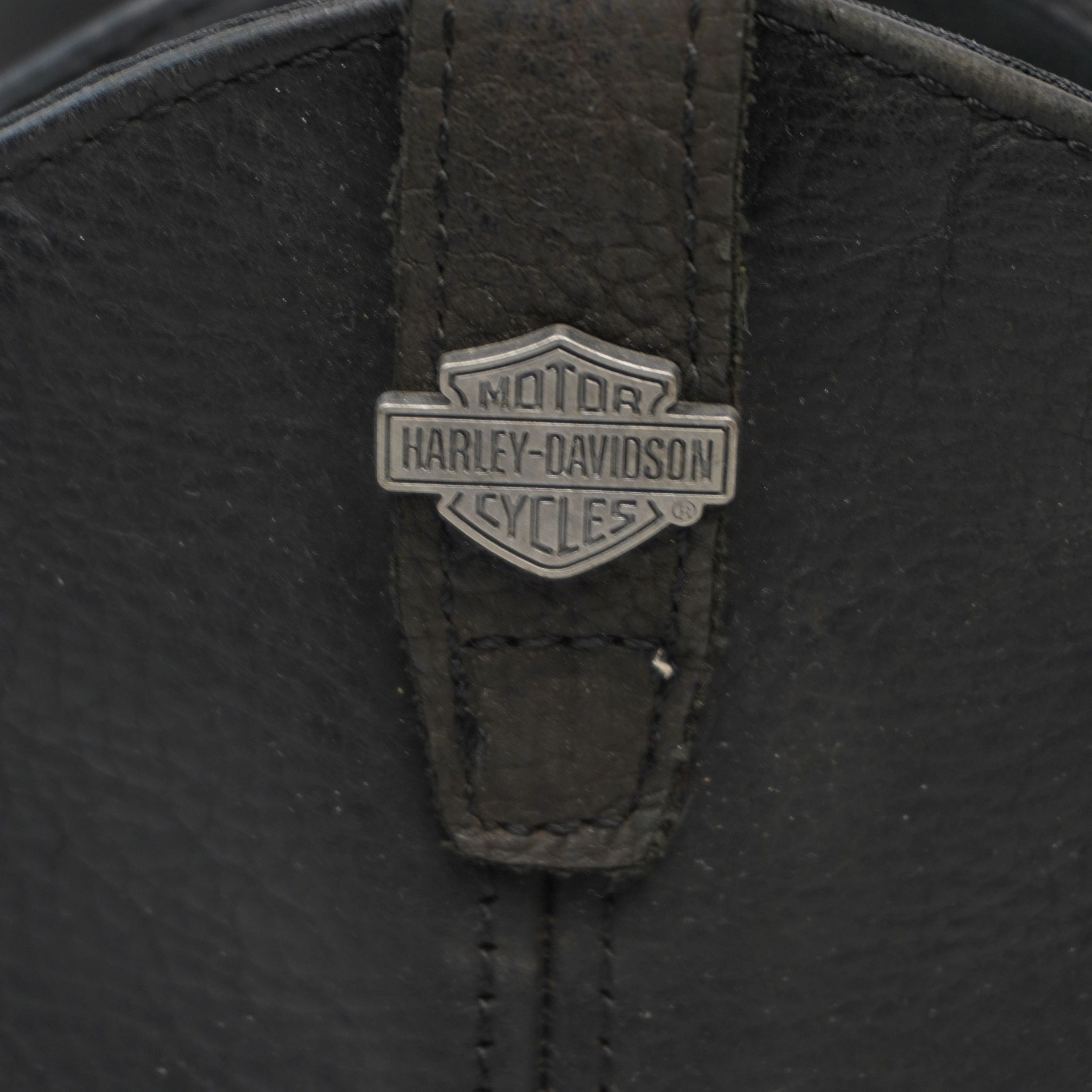 Macro della placchetta metallica argentata con logo ufficiale Bar and Shield di Harley-Davidson applicata sulla pelle.