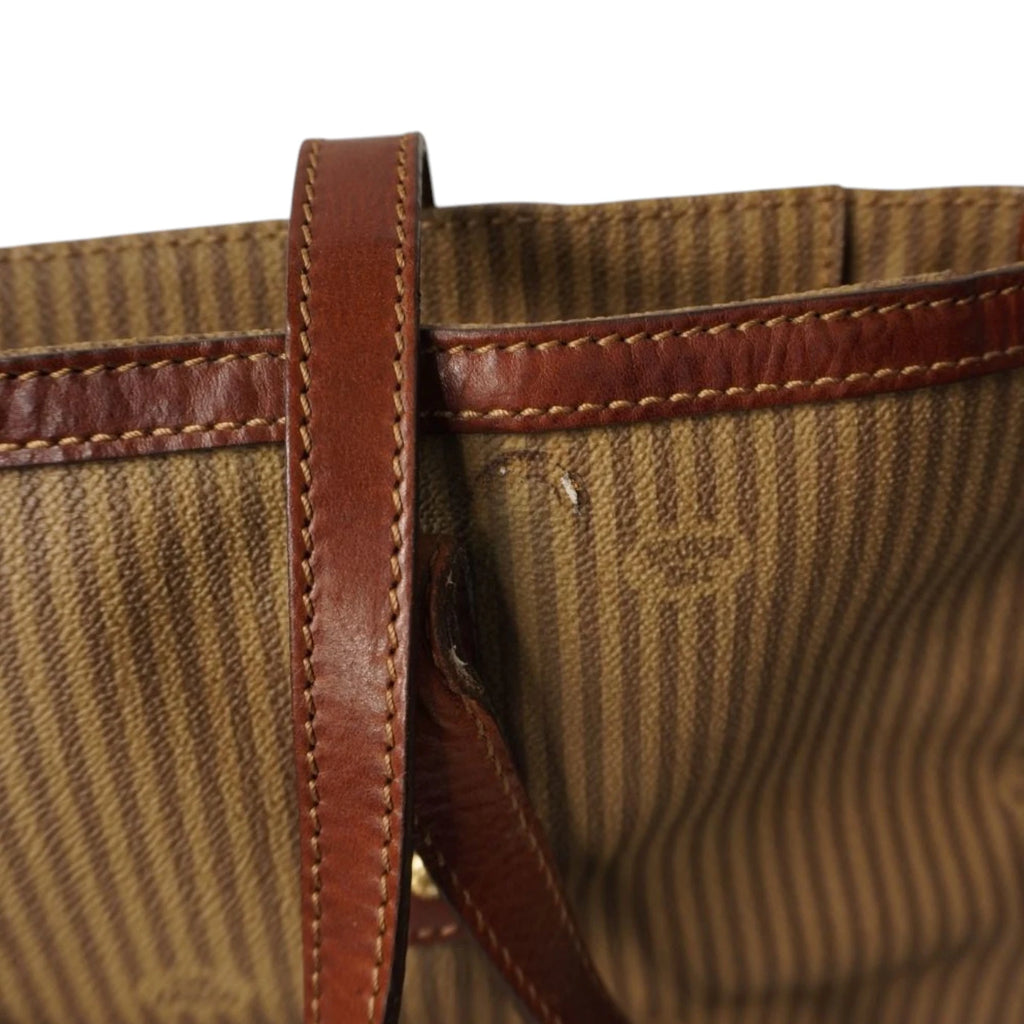 Dettaglio macro della patch ovale in pelle con logo The Bridge impresso a rilievo su tessuto jacquard a righe