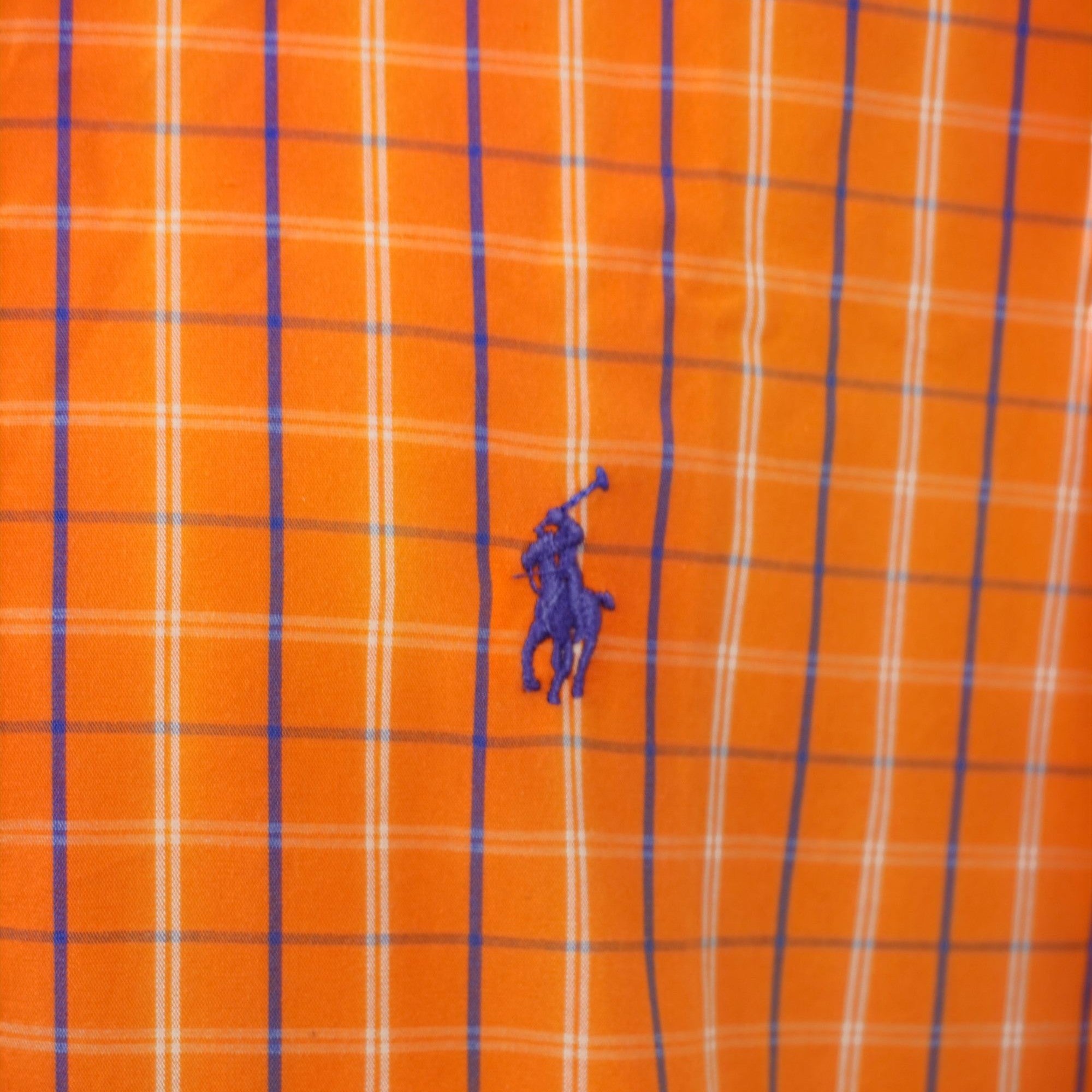 Primo piano dettagliato dell'iconico logo Polo Pony di Ralph Lauren ricamato in filo blu sul tessuto a quadri arancioni della camicia.