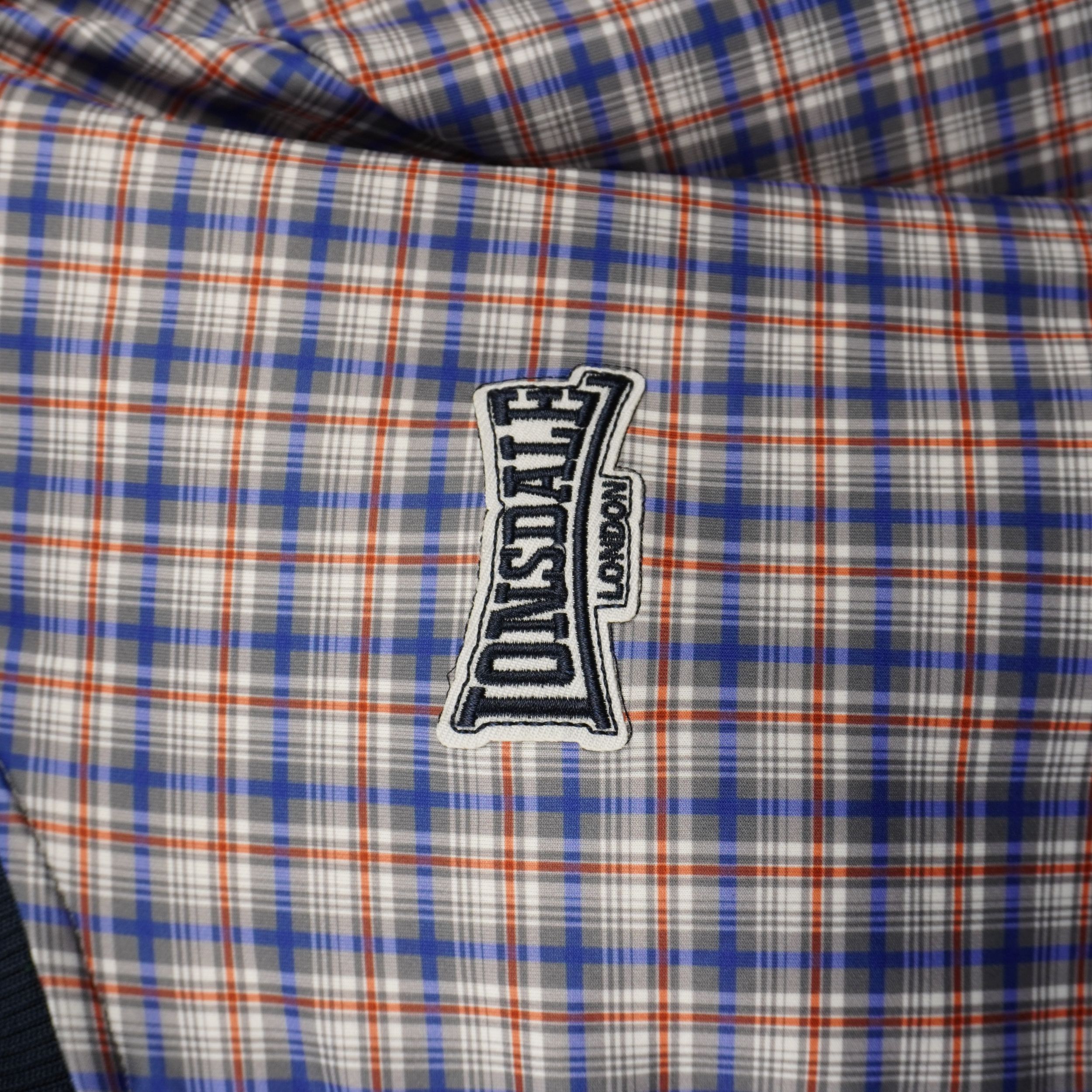 Dettaglio macro logo ricamato Lonsdale London applicato su giacca da uomo a quadri