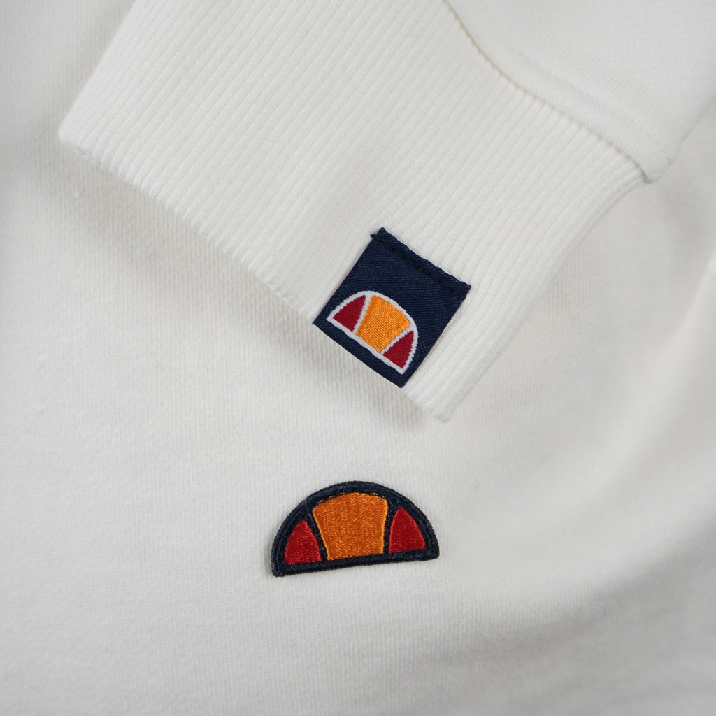 Primo piano ravvicinato del logo a semi-palla ellesse ricamato sul petto e del dettaglio sul polsino.