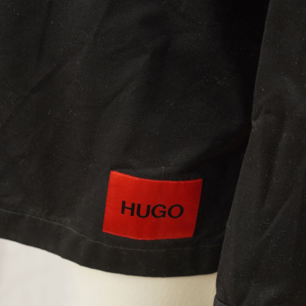 Primo piano dell'iconico logo rettangolare rosso HUGO applicato sul fondo laterale della giacca-camicia usata.