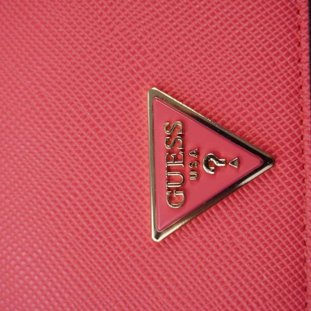 Primo piano della placca metallica a triangolo con logo Guess USA smaltata in tinta magenta con profili dorati lucidi.