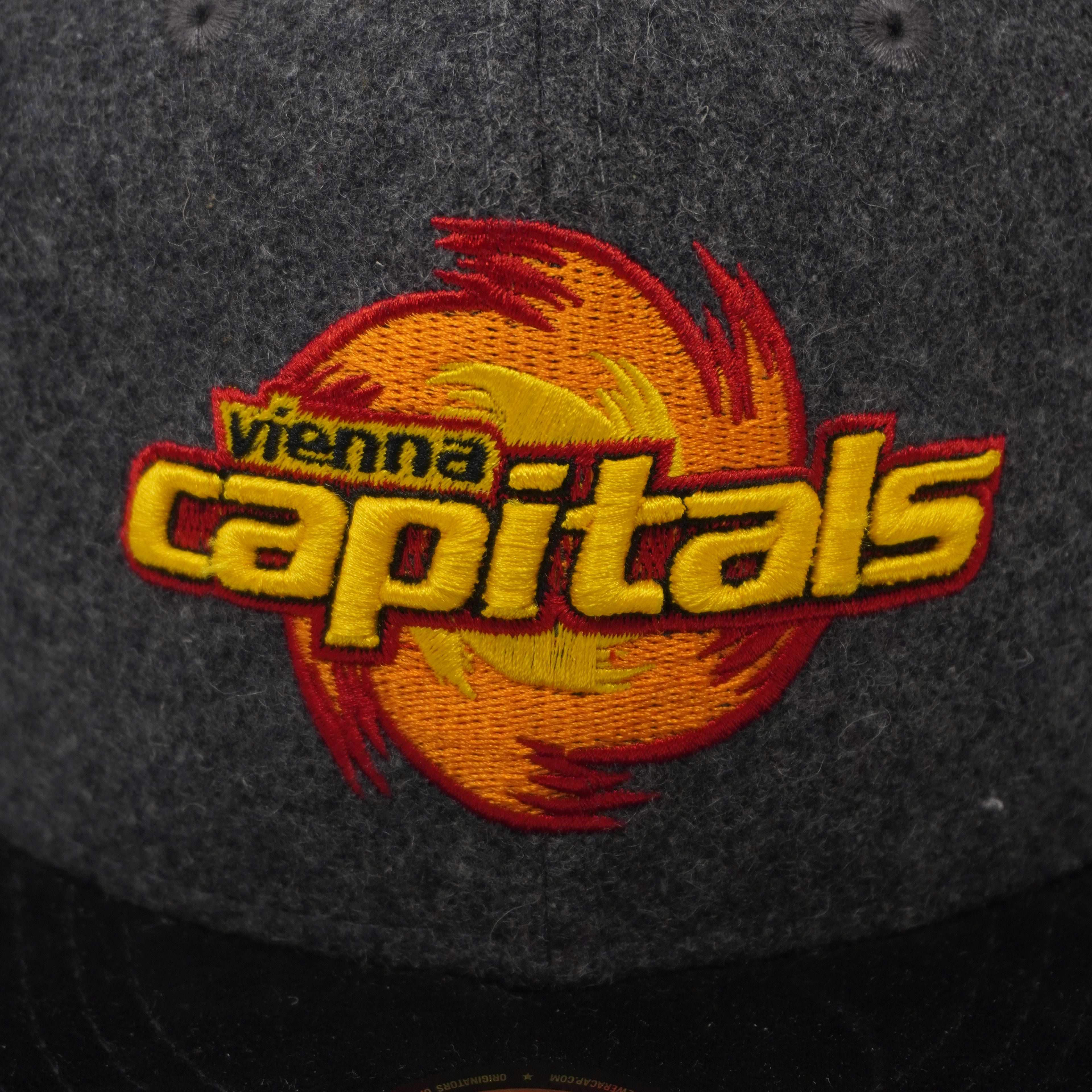 Macro del logo Vienna Capitals ricamato in 3D con filati giallo, arancione e nero su tessuto in misto lana grigio.
