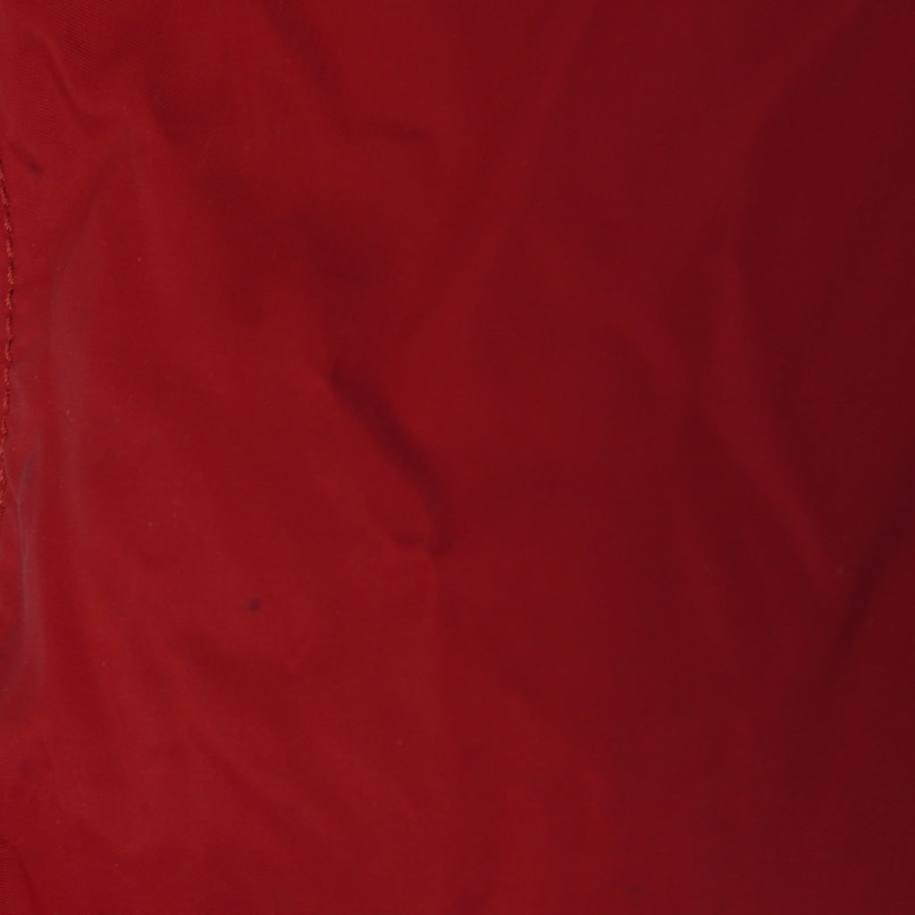 Foto di controllo a distanza ravvicinata che mostra una piccola e leggera macchia scura superficiale sul nylon rosso della borsa.