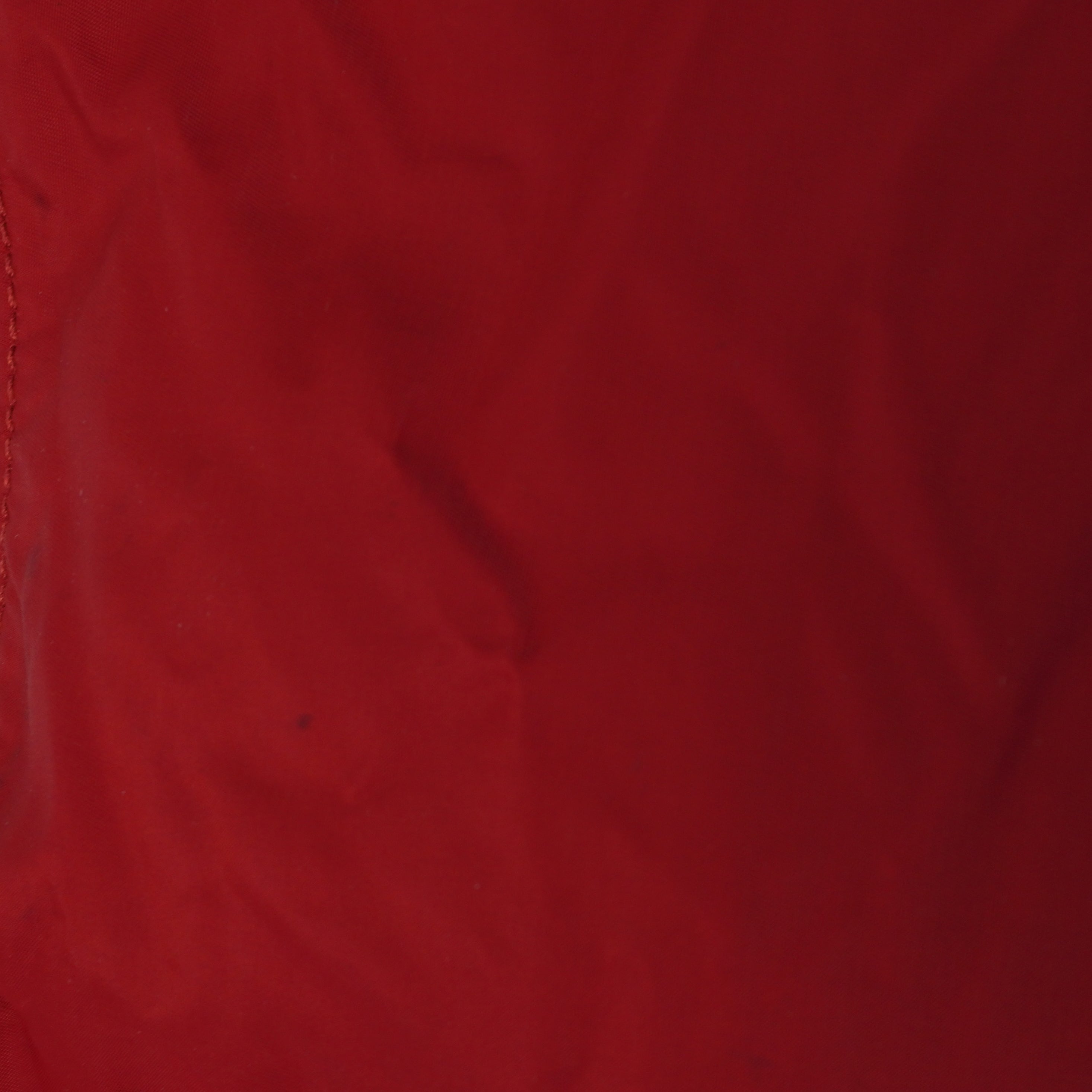 Foto di controllo a distanza ravvicinata che mostra una piccola e leggera macchia scura superficiale sul nylon rosso della borsa.