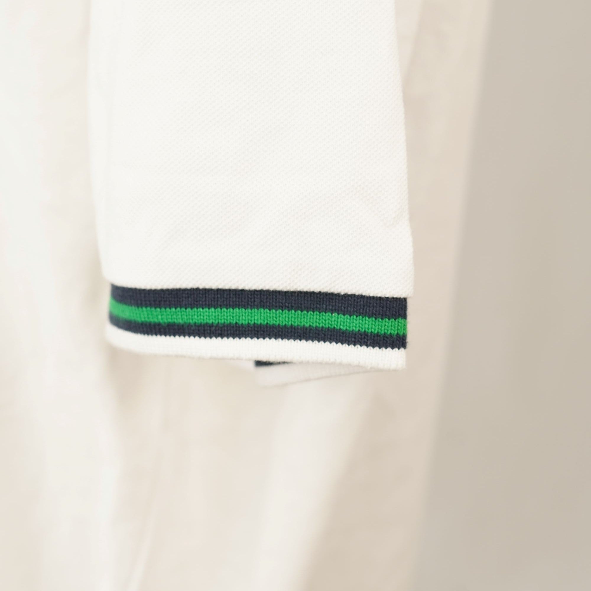 Dettaglio ravvicinato del bordo elasticizzato a costine della manica corta con righe colorate blu navy e verde brillante.