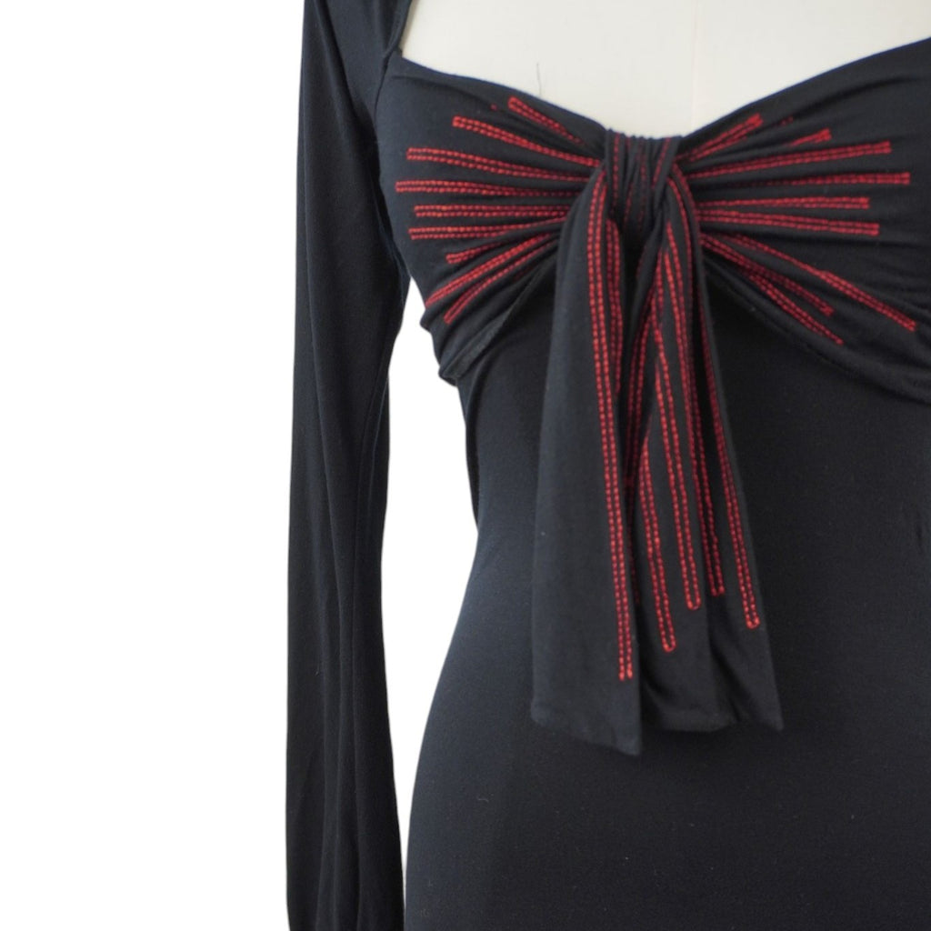  Inquadratura ravvicinata del maxi fiocco sul décolleté con righe verticali ricamate in filo rosso acceso a contrasto.