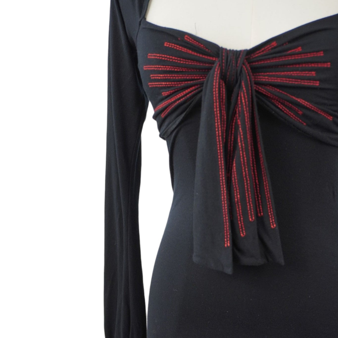  Inquadratura ravvicinata del maxi fiocco sul décolleté con righe verticali ricamate in filo rosso acceso a contrasto.