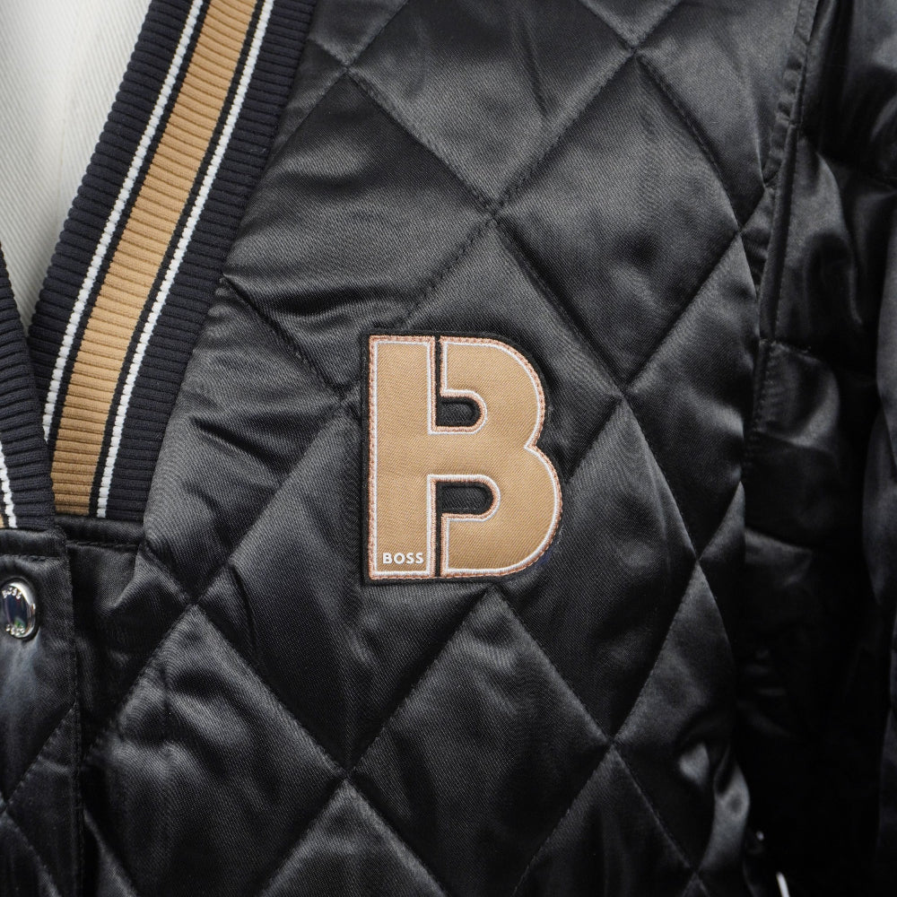 Primo piano della maxi patch con la lettera monogramma B ricamata in tessuto color oro e beige applicata sul petto del bomber.