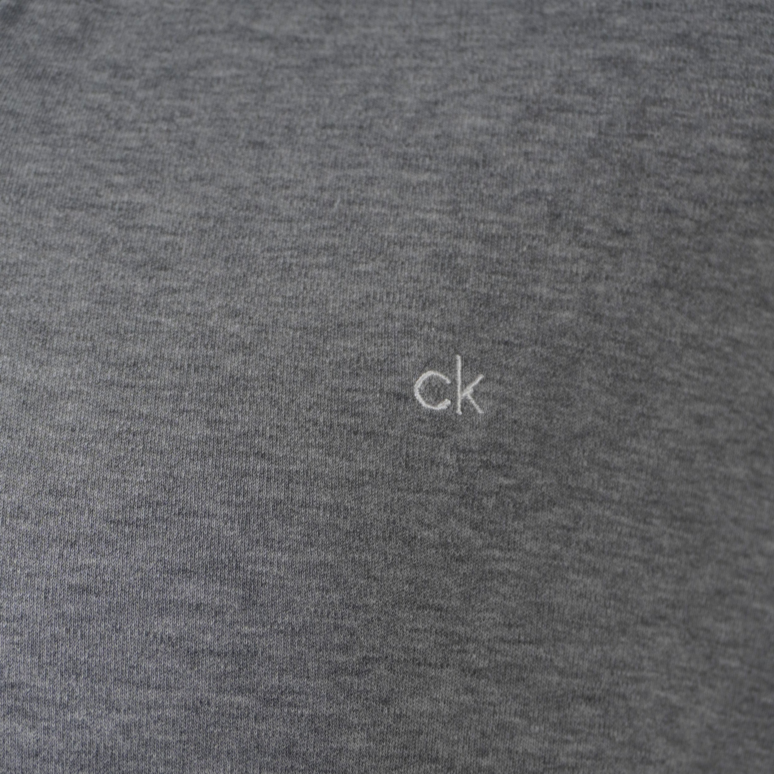 Primo piano ravvicinato del micro ricamo del logo ck sul petto della polo grigia Calvin Klein